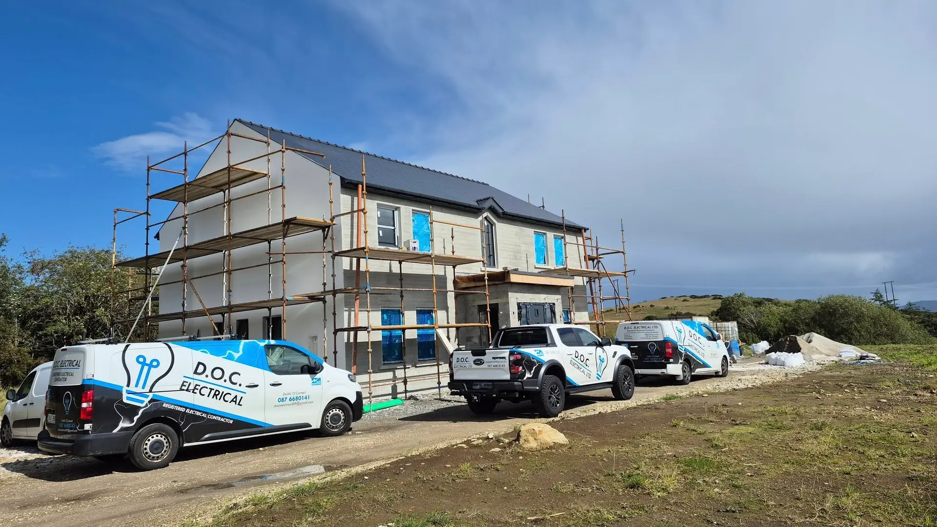 Fleet of four D.O.C Electrical branded vehicles parked at a new build house site with scaffolding in rural Donegal